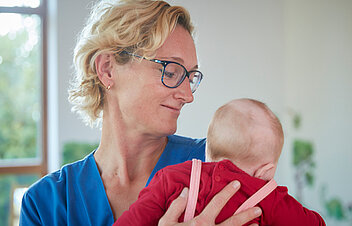 Picture: A nurse holds a child in her arms. The picture is linked to the rubric Care